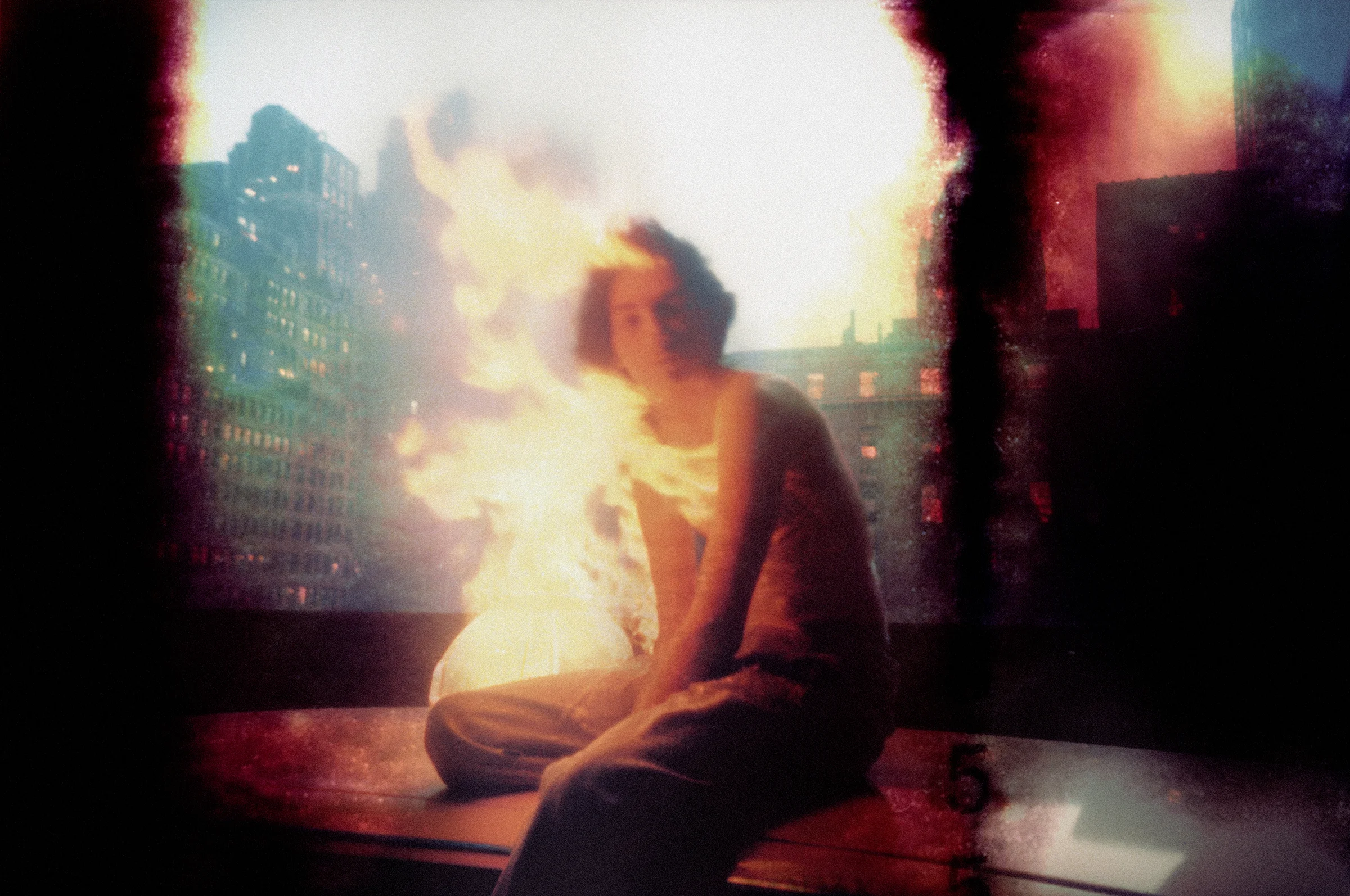 Burned photograph of a young man seated on a car roof and surrounded by flames, with New York City in the background. Visual generated by AI.